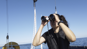 Tamara utilizando um binóculos em seu barco